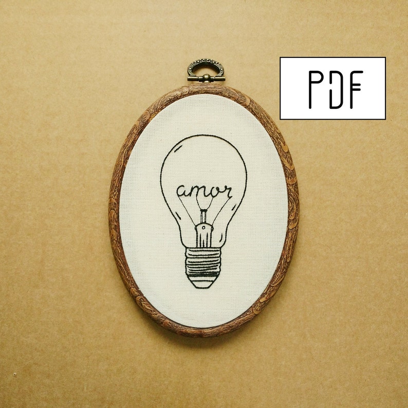 May include: An oval embroidery hoop with a light bulb design. The light bulb is black and contains the word "amor". The hoop has a wooden frame and a metal clasp. The word "PDF" is in a white box in the upper right corner.