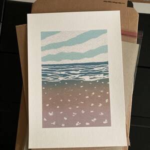 May include: A blue and white print of a seascape with a sandy beach and a blue sky with white clouds.