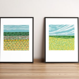 May include: Two framed prints of abstract landscape paintings. The left print features a green, red, and yellow field with a blue sky. The right print features a green field with a blue sky and white clouds.