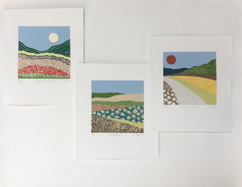 May include: Three landscape prints with a minimalist style. The first print features a red, green, and brown landscape with a white sun. The second print features a blue, green, and brown landscape with a yellow and blue flower field. The third print features a yellow, green, and brown landscape with a red sun.