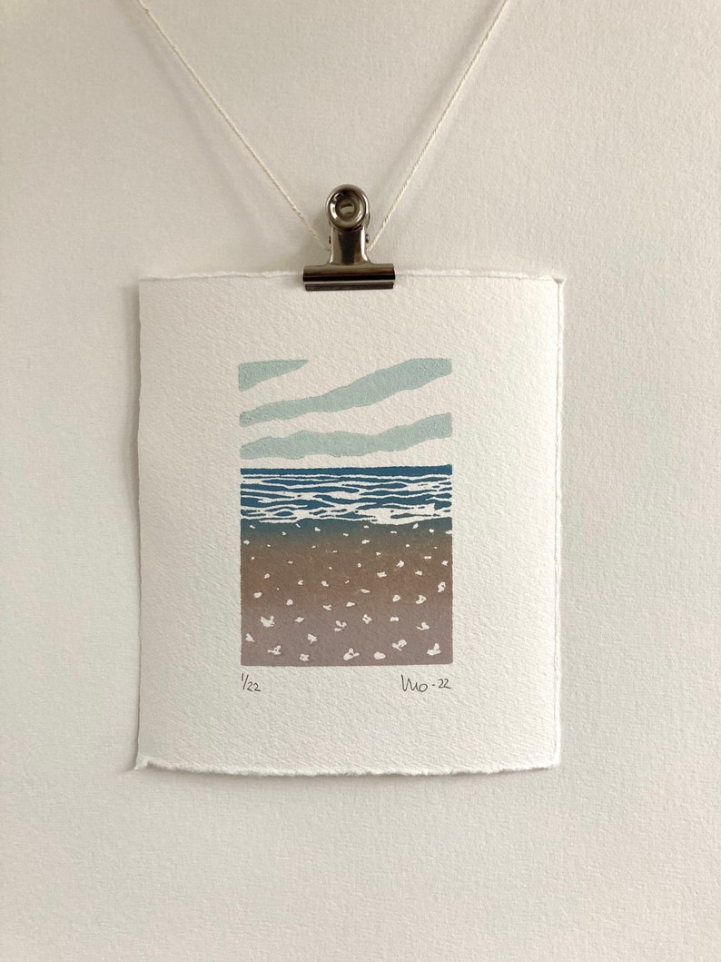 May include: A blue and white abstract print of a seascape with a brown sandy beach. The print is numbered 1/22 and dated Nov. 22.