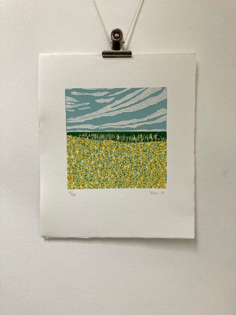 May include: A print of a landscape with a blue sky and white clouds above a field of yellow flowers. The print is numbered 19/20 and dated 2021.