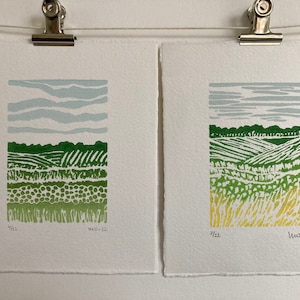 May include: Two framed prints of green and yellow landscape scenes with a blue sky. The prints are signed and dated "4/22" and "11.10.22".