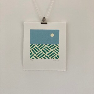 May include: A blue and green abstract print with a white circle in the upper portion of the blue section. The print is signed "23/26" and "11-20".