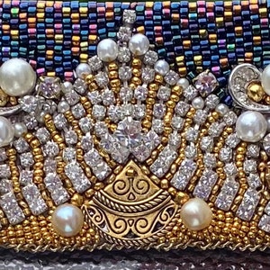 May include: A close-up of a beaded crown with gold and silver accents. The crown is made of small, iridescent beads and features a central design with a gold filigree pattern. The crown is adorned with white pearls and clear rhinestones.
