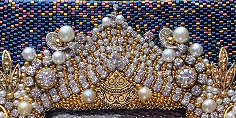 May include: A close-up of a beaded crown with gold and silver accents. The crown is made of small, iridescent beads and features a central design with a gold filigree pattern. The crown is adorned with white pearls and clear rhinestones.