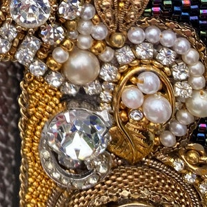May include: Close-up of a gold and silver beaded frame with white pearls and clear rhinestones. The frame is decorated with a gold leaf design.