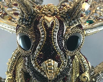 May include: Close-up of a jeweled insect sculpture with large black eyes, gold accents, and a burgundy body.
