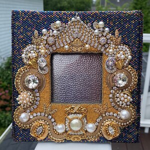 May include: A blue picture frame with a gold and pearl embellishment. The frame is decorated with rhinestones, pearls, and gold beads. The frame is perfect for displaying a special photo or artwork.