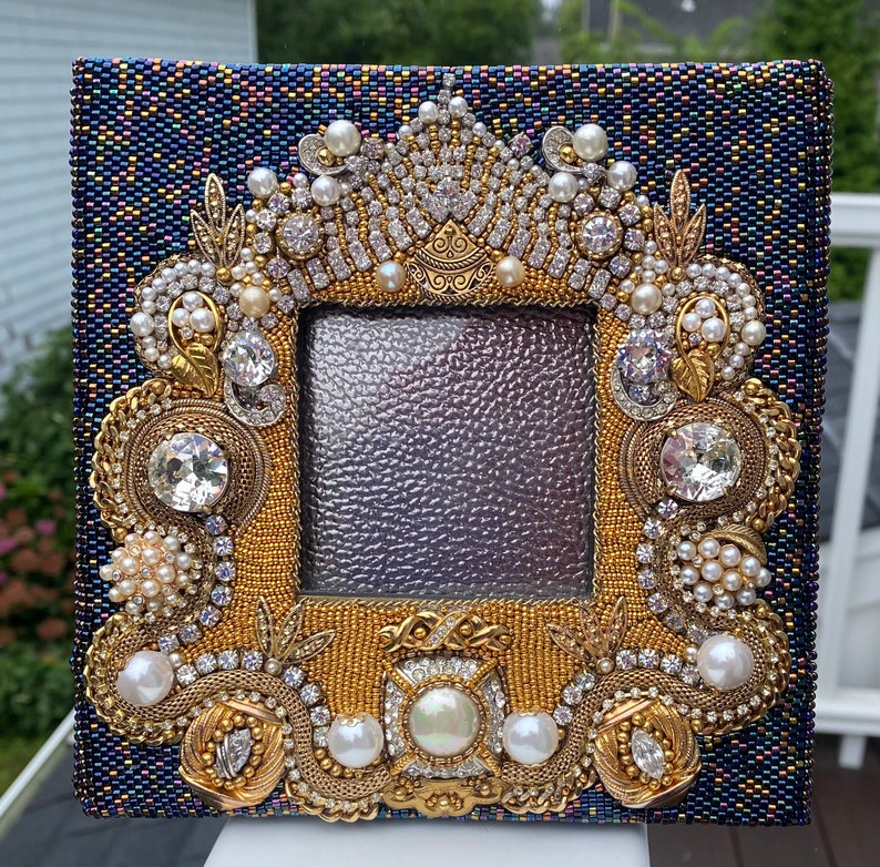 May include: A blue picture frame with a gold and pearl embellishment. The frame is decorated with rhinestones, pearls, and gold beads. The frame is perfect for displaying a special photo or artwork.