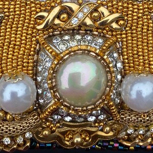 May include: A gold and white beaded clutch with a large pearl in the center. The clutch is decorated with intricate beadwork and a gold chain.