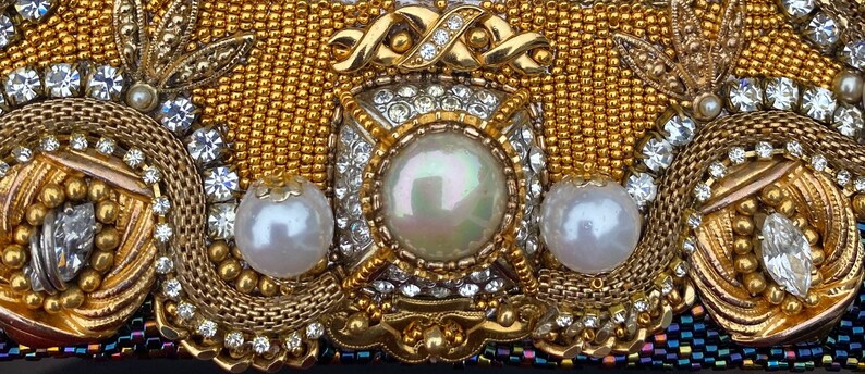 May include: A gold and white beaded clutch with a large pearl in the center. The clutch is decorated with intricate beadwork and a gold chain.