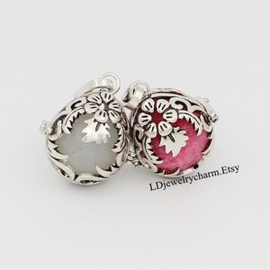 May include: Two silver charm pendants with a floral design. One pendant has a white interior and the other has a pink interior. The pendants are both round and have a delicate floral design.