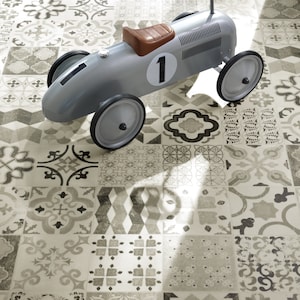 Puede incluir: Un coche de juguete plateado con un asiento de cuero marrón y un número negro "1" en el lateral. El coche está sobre un suelo de baldosas blancas y grises con un patrón.