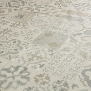 Puede incluir: Un suelo de baldosas estampadas con un diseño de patchwork. Las baldosas presentan varios patrones geométricos y florales en tonos grises, beige y blanco. El suelo tiene una estética vintage o antigua, con un aspecto ligeramente desgastado.