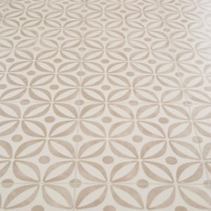 May include: Off-white and tan patterned tile flooring. The design features a repeating pattern of stylized floral shapes and small circles. The tiles are arranged in a grid, creating a cohesive and decorative surface.