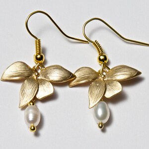 May include: Gold earrings with a flower design and a pearl dangle. The flowers are a brushed gold finish.