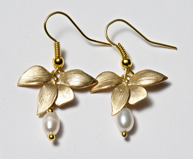 May include: Gold earrings with a flower design and a pearl dangle. The flowers are a brushed gold finish.