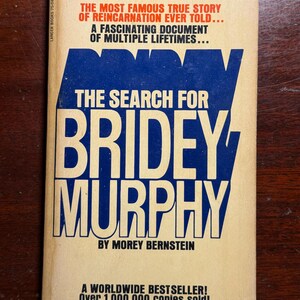 May include: A vintage paperback book titled The Search for Bridey Murphy by Morey Bernstein. The cover is cream-colored with bold blue text and black lettering. It features the phrases New, Revised Edition, First Time in Paperback, and A Worldwide Bestseller.