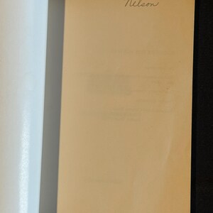 Puede incluir: Libro abierto con una p&aacute;gina beige y la palabra manuscrita "Nelson" en cursiva en la esquina superior derecha. El lado izquierdo del libro muestra p&aacute;ginas blancas. El fondo es negro.
