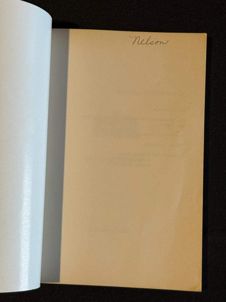 Puede incluir: Libro abierto con una p&aacute;gina beige y la palabra manuscrita "Nelson" en cursiva en la esquina superior derecha. El lado izquierdo del libro muestra p&aacute;ginas blancas. El fondo es negro.