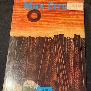 May include: A book cover with the title "Max Ernst" in blue text. The cover features a red and orange sunset with a black circle in the center. The bottom of the cover shows a dark forest with a white cat and the word "TASCHEN" in blue text.