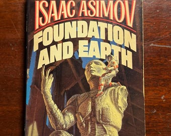 May include: A paperback book cover featuring a science fiction illustration of a large, stone-like figure with a smaller figure standing on its shoulder. The title of the book is "Foundation and Earth" by Isaac Asimov. The book is part of the classic Foundation series.