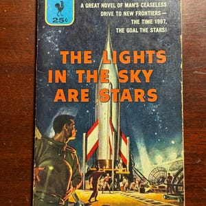May include: Vintage paperback book cover for "The Lights in the Sky Are Stars" by Fredric Brown. The cover features a rocket ship, figures, and the title in orange against a starry night sky. The Bantam Books logo is in the upper left corner.
