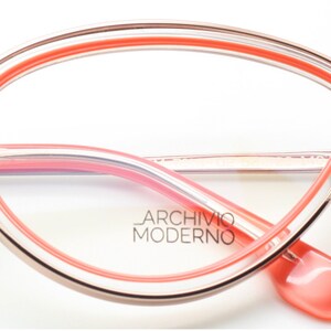 May include: Rose gold cat-eye glasses with a pink and clear frame. The brand name "Archivio Moderno" is printed on the frame.