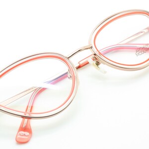 May include: A pair of pink and gold cat eye glasses with a double rim. The brand name "ARCHIVIO MODERNO" is printed on the right temple.