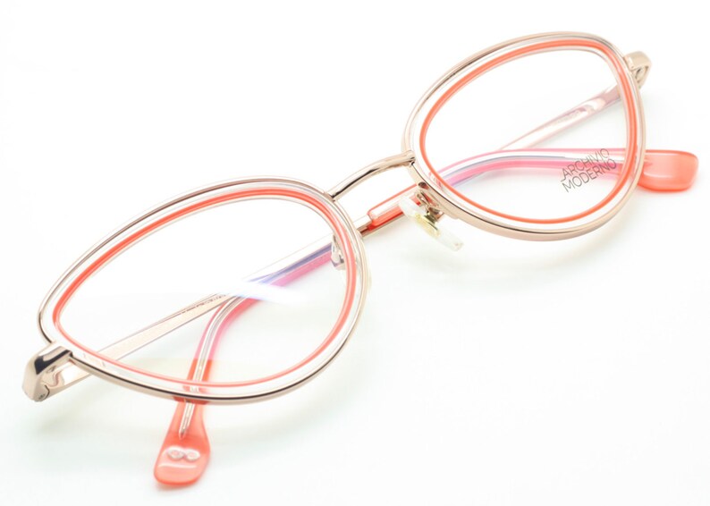 May include: A pair of pink and gold cat eye glasses with a double rim. The brand name "ARCHIVIO MODERNO" is printed on the right temple.