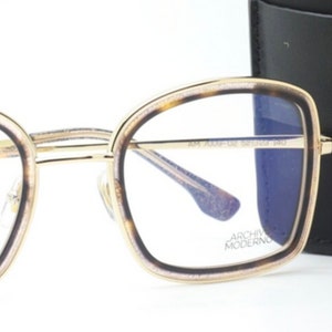May include: Gold-rimmed eyeglasses with a tortoise shell frame and blue tinted lenses. The glasses are shown with a black leather case with the text "ARCHIVIO MODERNO" printed on it.