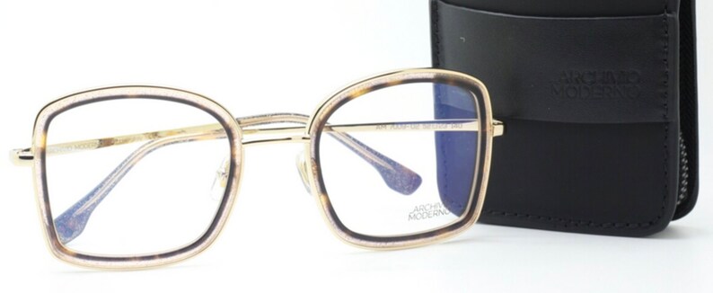 May include: Gold-rimmed eyeglasses with a tortoise shell frame and blue tinted lenses. The glasses are shown with a black leather case with the text "ARCHIVIO MODERNO" printed on it.