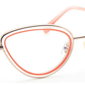 May include: Gold-tone cat-eye glasses with a bright orange accent around the lenses.