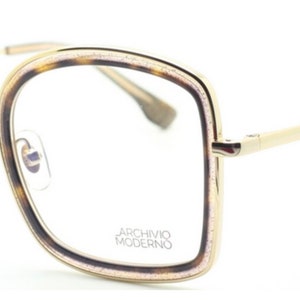 May include: Gold-rimmed eyeglasses with a tortoise shell frame and clear lenses. The frame has a subtle sparkle and the arms are gold metal. The brand name "Archivio Moderno" is printed on the frame.