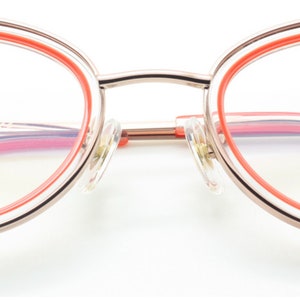 May include: Gold-tone cat-eye glasses with a pink and orange double rim. The glasses have a clear lens and the brand name "ARCHIVIO MODERNO" is printed on the right lens.