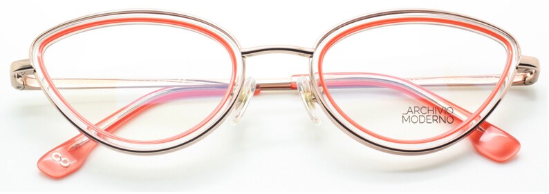 May include: Gold-tone cat-eye glasses with a pink and orange double rim. The glasses have a clear lens and the brand name "ARCHIVIO MODERNO" is printed on the right lens.