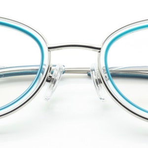 May include: Silver cat-eye glasses with a blue trim around the lenses. The brand name "Archivio Moderno" is printed on the right temple.