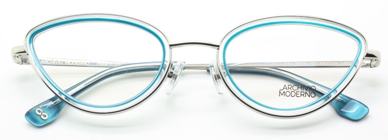 May include: Silver cat-eye glasses with a blue trim around the lenses. The brand name "Archivio Moderno" is printed on the right temple.
