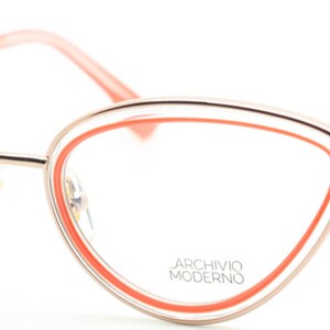 May include: Cat-eye shaped eyeglasses with a gold metal frame and a bright orange accent around the lenses. The brand name "Archivio Moderno" is printed on the right lens.