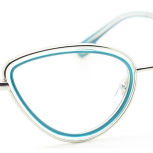 May include: Silver cat-eye glasses with a blue trim around the lenses. The brand name "ANNA KARIN" is printed on the right temple.