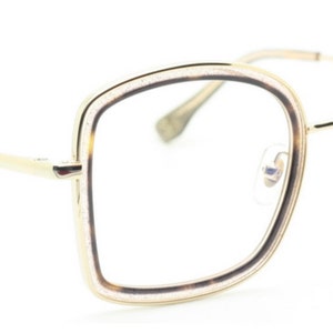 May include: Gold-tone eyeglasses with a square frame and brown tortoise shell accents. The frame has a double rim design.