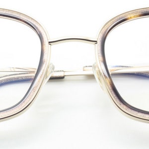 May include: Gold-rimmed eyeglasses with a tortoise shell frame. The lenses are clear and the frame has a subtle sparkle. The brand name "Archivio Moderno" is printed on the right lens.