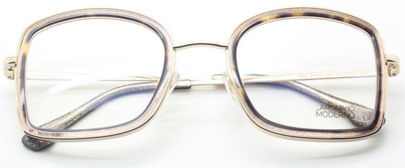 May include: Gold-rimmed eyeglasses with a tortoise shell frame. The lenses are clear and the frame has a subtle sparkle. The brand name "Archivio Moderno" is printed on the right lens.