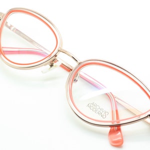 May include: Rose gold cat eye glasses with a pink and orange double rim. The glasses have the text "ARCHIVIO MODERNO" on the right lens.