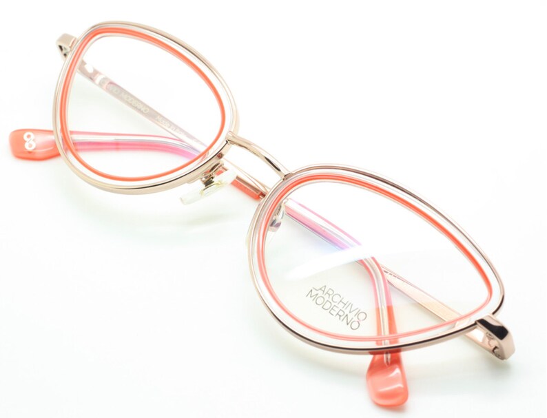 May include: Rose gold cat eye glasses with a pink and orange double rim. The glasses have the text "ARCHIVIO MODERNO" on the right lens.