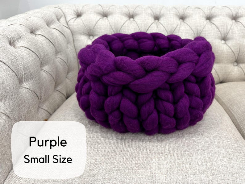May include: A deep purple basket crafted from thick, chunky yarn in a braided knit pattern. The basket features a round, open-top design with a soft, textured appearance. A white label in the corner displays the text Purple Small Size.