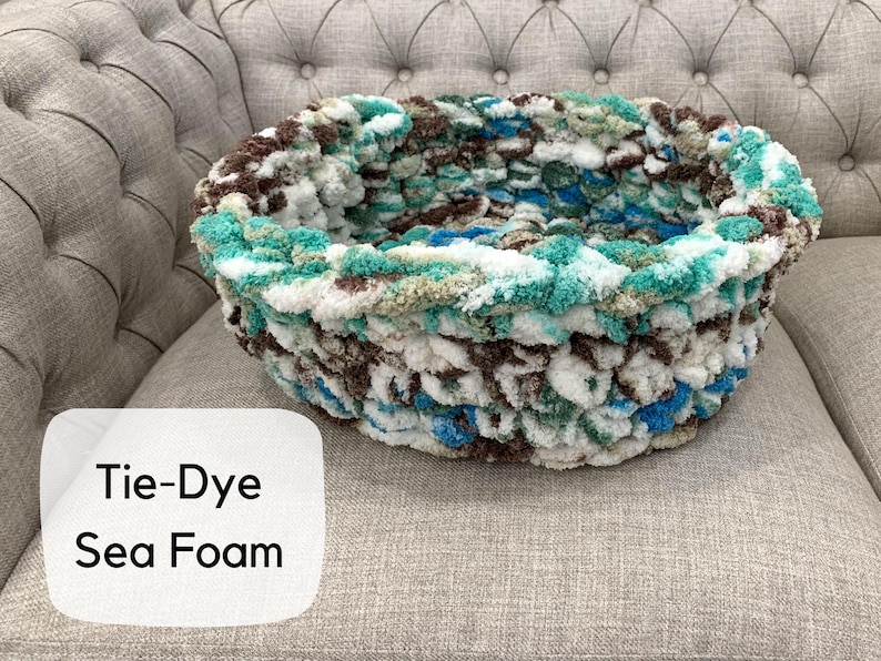 Puede incluir: Una cama redonda para mascotas te&ntilde;ida con tintes en colores espuma de mar. La cama est&aacute; hecha de un material suave y texturizado con tonos de blanco, azul, marr&oacute;n y verde. El texto "Tie-Dye Sea Foam" est&aacute; en un cuadro blanco.
