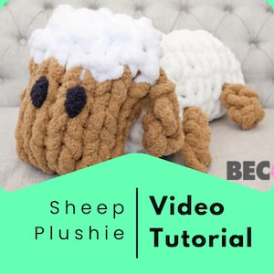 May include: A brown and white knitted sheep plushie with black eyes. The plushie is lying on a white sofa. The text "Sheep Plushie | Video Tutorial" is on a green background.