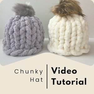 May include: Two chunky knit hats with faux fur pom poms. One hat is light gray and the other is white. The image includes the text "Chunky Hat Video Tutorial".